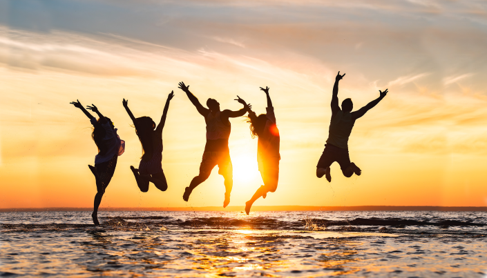5 adult silhouettes jumping up with their arms up at the back as the sun is setting