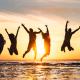 5 adult silhouettes jumping up with their arms up at the back as the sun is setting