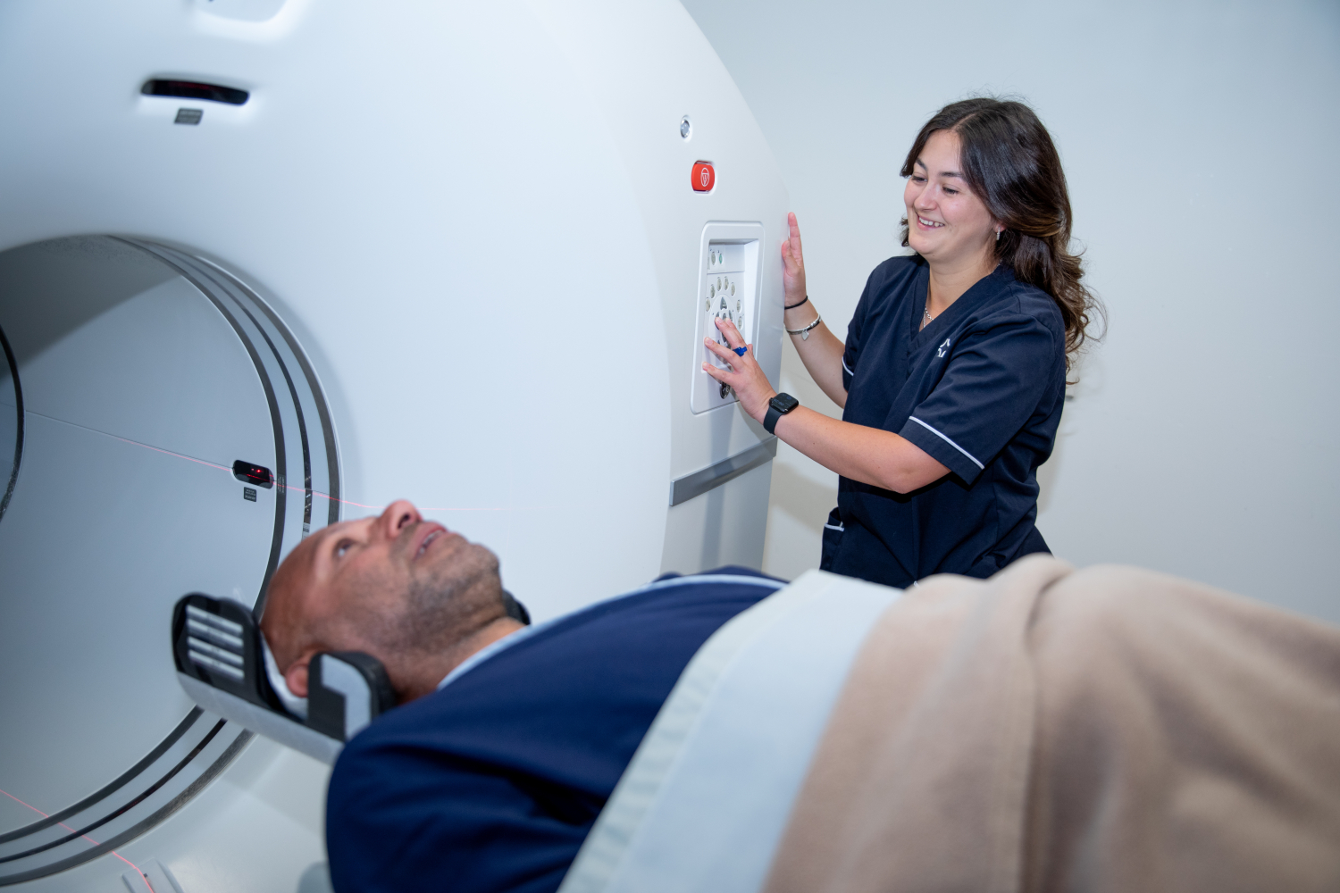 Patient undergoing a CT scan while a radiology technician operates the medical imaging equipment in a diagnostic healthcare facility.